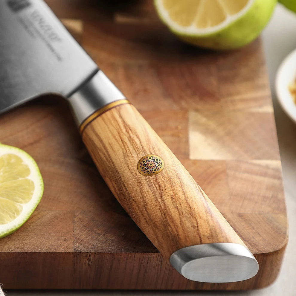 Notre couteau Santoku en acier Damas est rehaussé d’une petite fleur en cuivre, subtilement incrustée dans une poignée en bois d'olivier, affirmant son caractère noble, chaleureux et luxueux et son raffinement artisanal.
